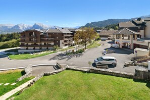 Un hotel con estacionamiento, edificio de recepción y montañas al fondo.