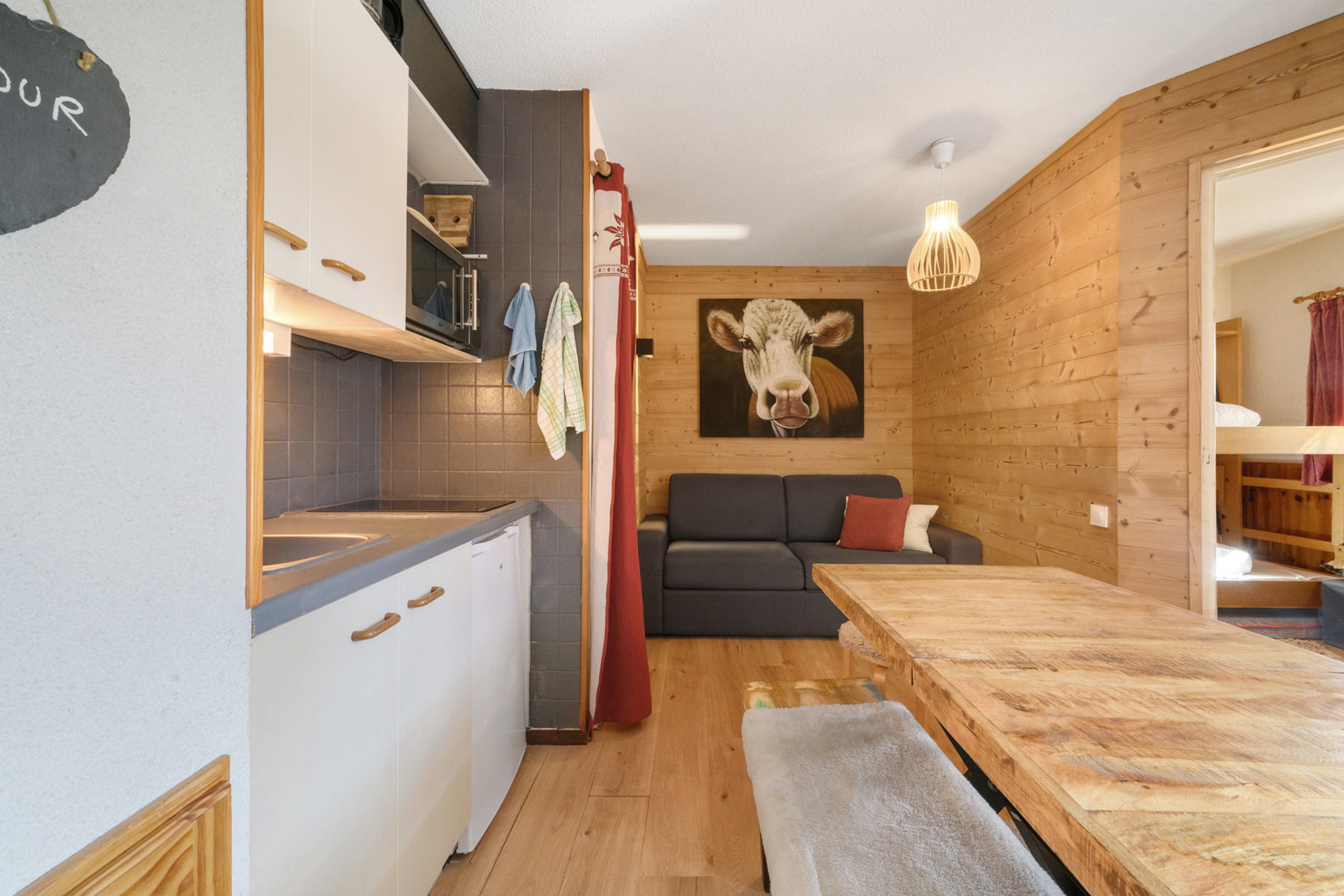 A compact living space with a kitchenette, a dining area, a sofa, and a cow painting on the wall.