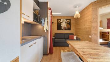 A compact living space with a kitchenette, a dining area, a sofa, and a cow painting on the wall.