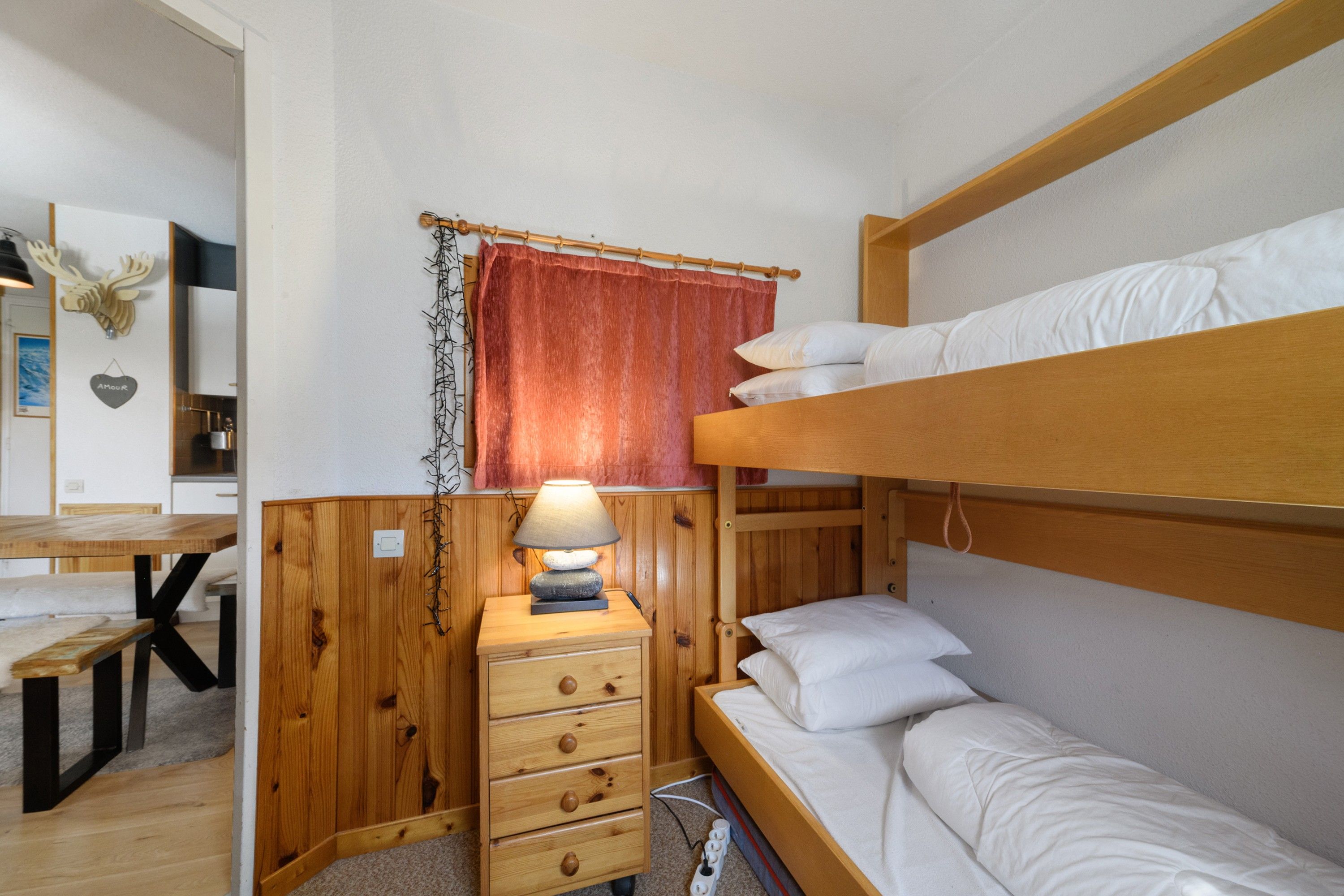 Ein Etagenbett mit Holz Kopfteil, ein Nachttisch mit Lampe und eine kleine Kommode mit Schubladen.