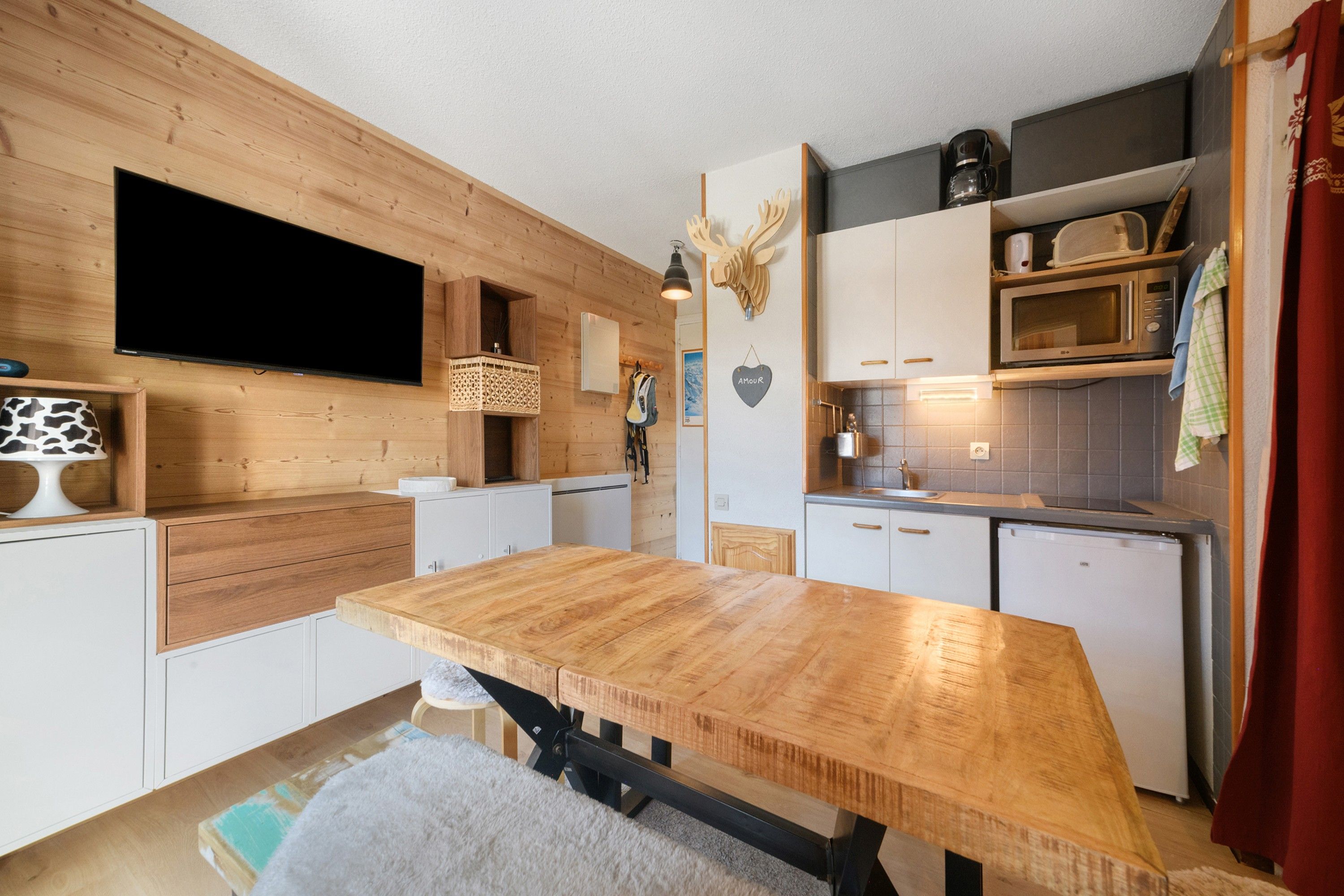 A modern kitchen with wooden cabinetry, a wooden dining table, and a mounted television.