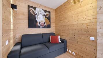 Ein modernes Interieur mit einer Holzpaneelausstattung, einem schwarzen Sofa, einem roten Kissen und einem Gemälde mit einer Kuh.