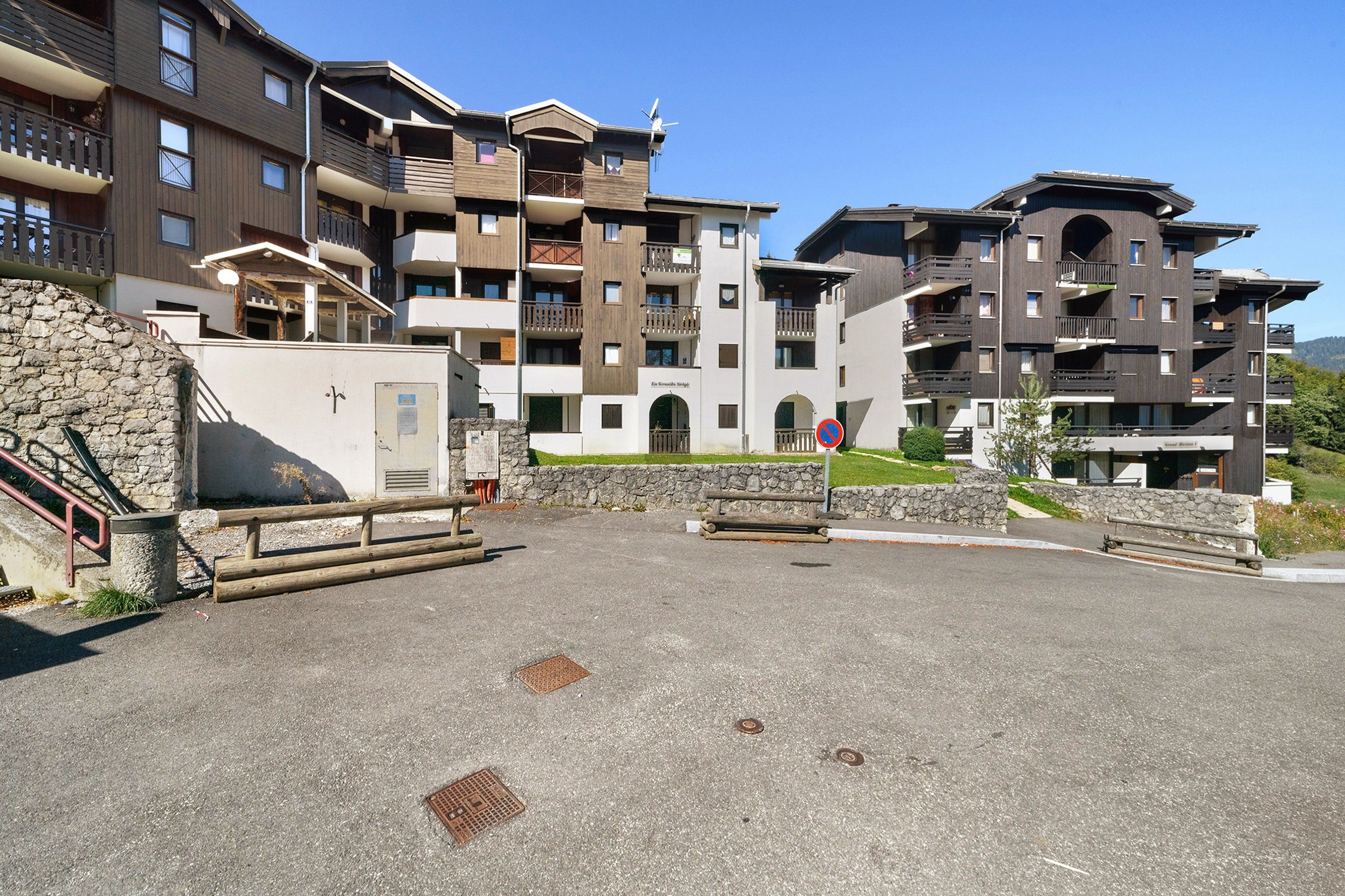 A multi-story hotel with balconies, a stone wall, and a paved courtyard.