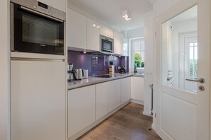 A modern kitchen with white cabinets, a microwave, and a coffee maker. - Beach Love Sylt, Germany (Sylt)