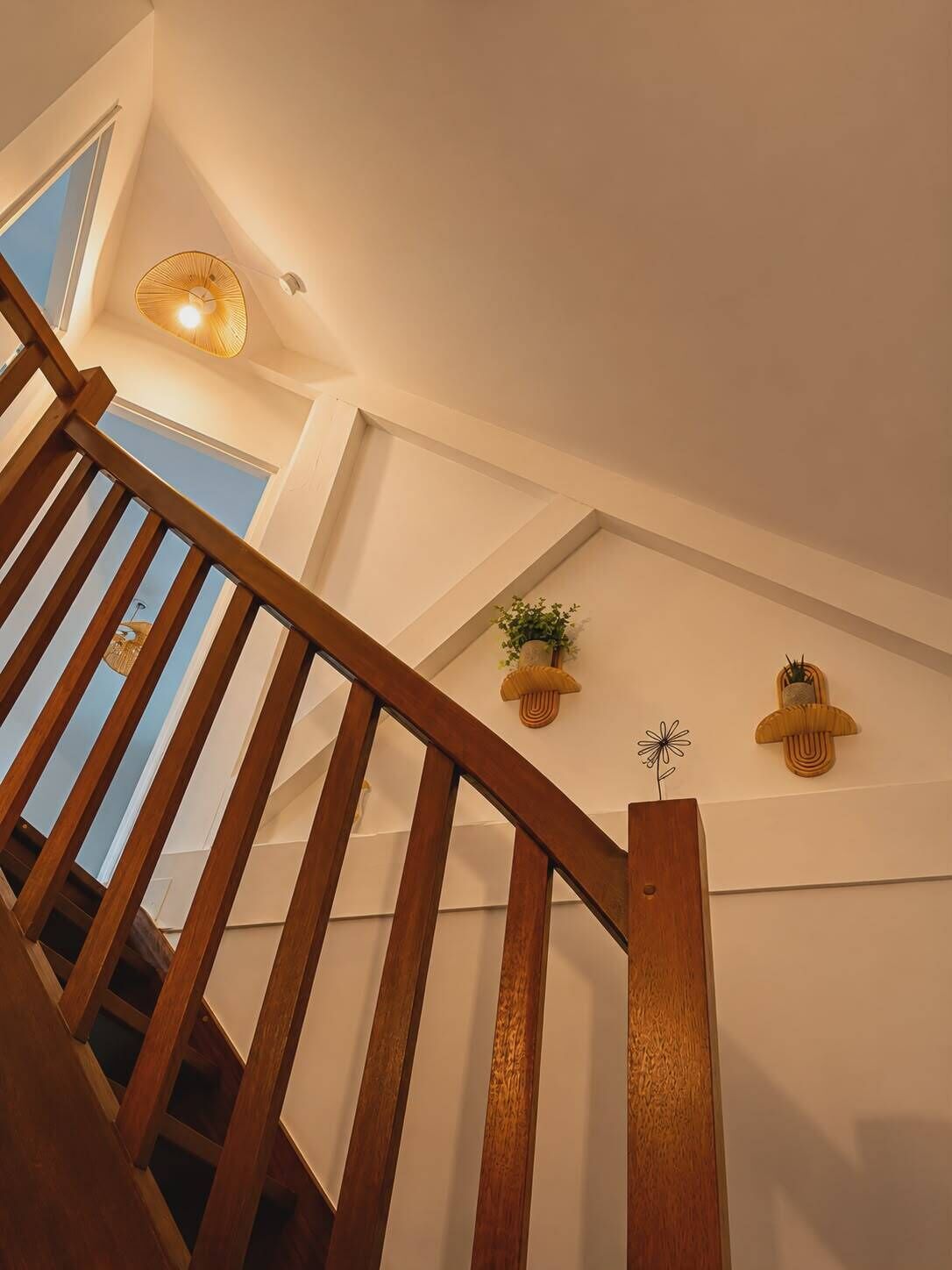 A wooden staircase with a view of the sky through a window, a wall-mounted light fixture, and two wall-mounted planters with plants.