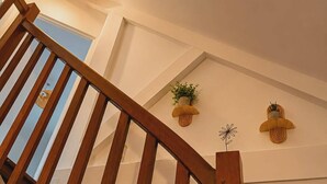 Eine Holztreppe mit Blick auf den Himmel durch ein Fenster, einer an der Wand befestigten Leuchte und zwei Wandpflanzgefäße mit Pflanzen.
