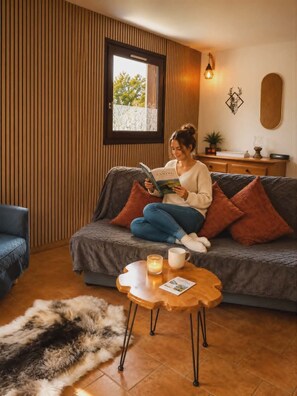 A cozy living room with a sofa, a coffee table, and a window with a view of greenery. - Nature Lodge **** Monts du Cantal - Le Violon Cantal Emotion (Valette)