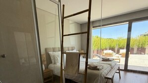 Ein modernes Schlafzimmer mit Glastrennwand, einer Holzleiter, einem Bett mit weißen Leinen und Blick auf einen Garten.