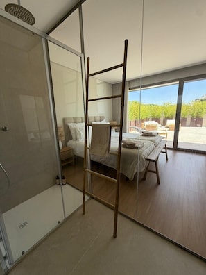 Ein modernes Schlafzimmer mit Glastrennwand, einer Holzleiter, einem Bett mit weißen Leinen und Blick auf einen Garten.