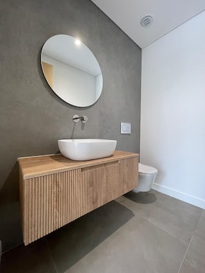 Ein modernes Badezimmer mit rundem Spiegel, einem Aufsatzwaschbecken und einer Toilette.