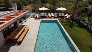 Ein Pool mit Liegestühlen und Sonnenschirmen, umgeben von Grünflächen und Gebäuden.