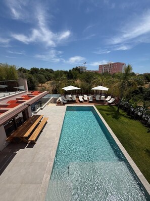 Ein Pool mit Liegestühlen und Sonnenschirmen, umgeben von Grünflächen und Gebäuden.