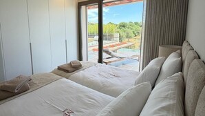 Ein modernes Schlafzimmer mit einem großen Bett, einer Sitzecke und Blick auf einen Pool und Grünflächen.