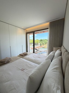 Ein modernes Schlafzimmer mit einem großen Bett, einer Sitzecke und Blick auf einen Pool und Grünflächen.