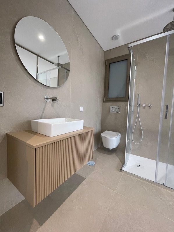 Ein modernes Badezimmer mit rundem Spiegel, einem rechteckigen Waschbecken, einer Toilette und einer Duschkabine.