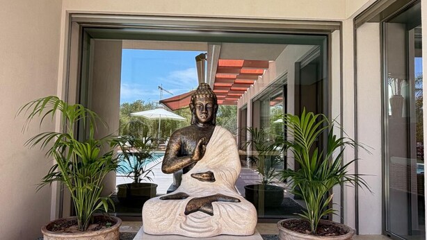 Eine Statue einer sitzenden Figur mit einer Tafel, auf der 'MOMENTS BY THE SEA' steht, vor einem Gebäudeeingang.