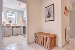 Eine moderne Küche mit weißen Schränken, einem Geschirrspüler und einem Herd. In der Ecke steht eine Holzkiste und an der Wand ein Heizkörper.