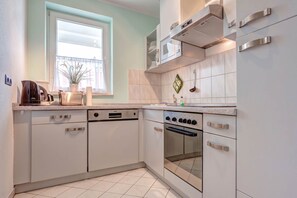 Eine moderne Küche mit weißen Schränken, einem Einbauofen, einem Geschirrspüler und einem Fenster mit Jalousien.