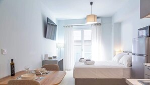 A compact hotel room with a bed, a small kitchenette, a dining area with a table and chairs, a TV mounted on the wall, and a window with curtains. - Studio 4 Kalamata - Bright Escape in the Centre (Kalamata)