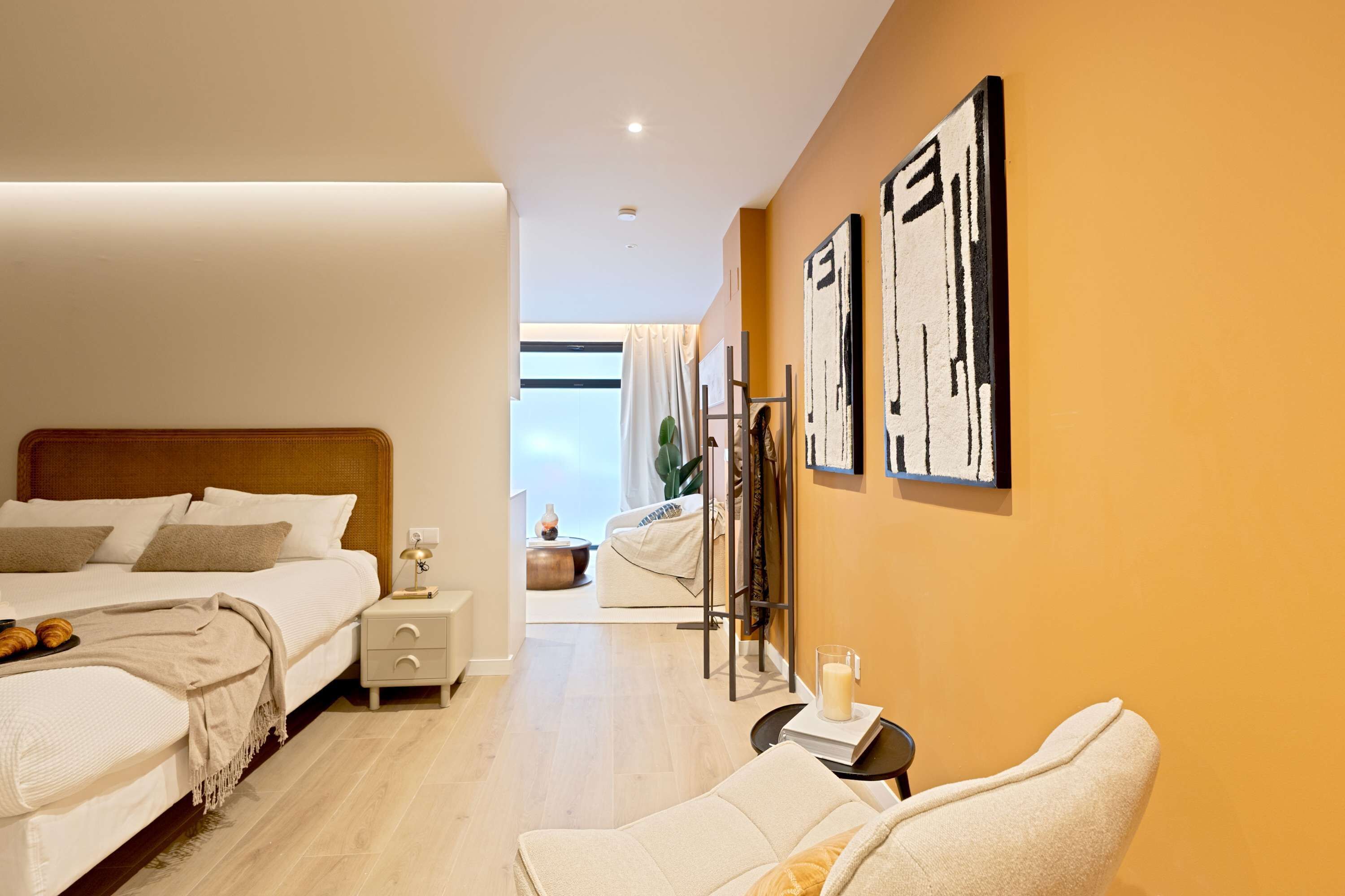 Una habitación de hotel moderna con una cama grande, mesitas de noche, un área de descanso y obras de arte en las paredes.