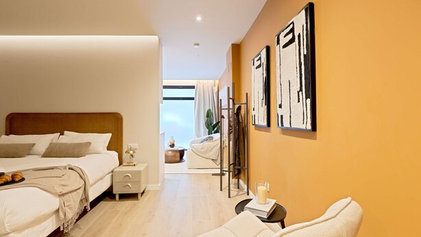 Una habitación de hotel moderna con una cama grande, mesitas de noche, un área de descanso y obras de arte en las paredes.