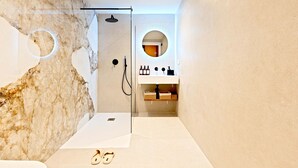 Un baño moderno con pared de mármol, ducha envuelta en vidrio, lavabo con espejo y perchero para toallas.