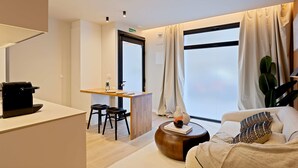 Una habitación de hotel moderna con escritorio, sofá, un ventanal con cortinas y una planta.