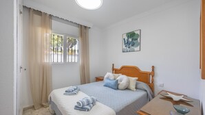 Ein Schlafzimmer mit einem Bett, einem Nachttisch, einem Fenster mit Vorhängen, einem Wandbild und einer Tür.