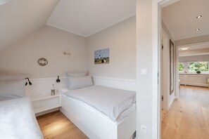 A bedroom with two beds, a nightstand, a wall-mounted lamp, and a painting. - Dolles Hüs - Dolles Hüs – Stylish family vacation home with a garden in (Wenningstedt-Braderup (Sylt))