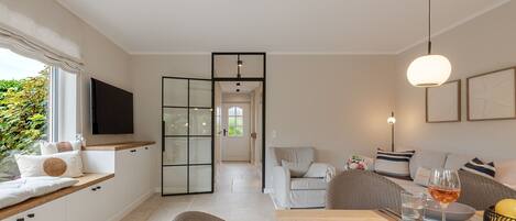 A modern living room with a sofa, a dining table, and a TV mounted on the wall.
