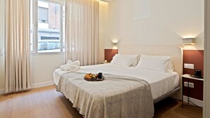 Hotellihuone, jossa on suuri sänky, yöpöytä lampun kanssa ja ikkuna, jossa on verhot.