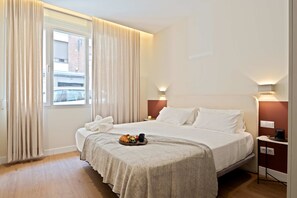 Ein Hotelzimmer mit einem großen Bett, einem Nachttisch mit Lampe und einem fenster mit Vorhängen.