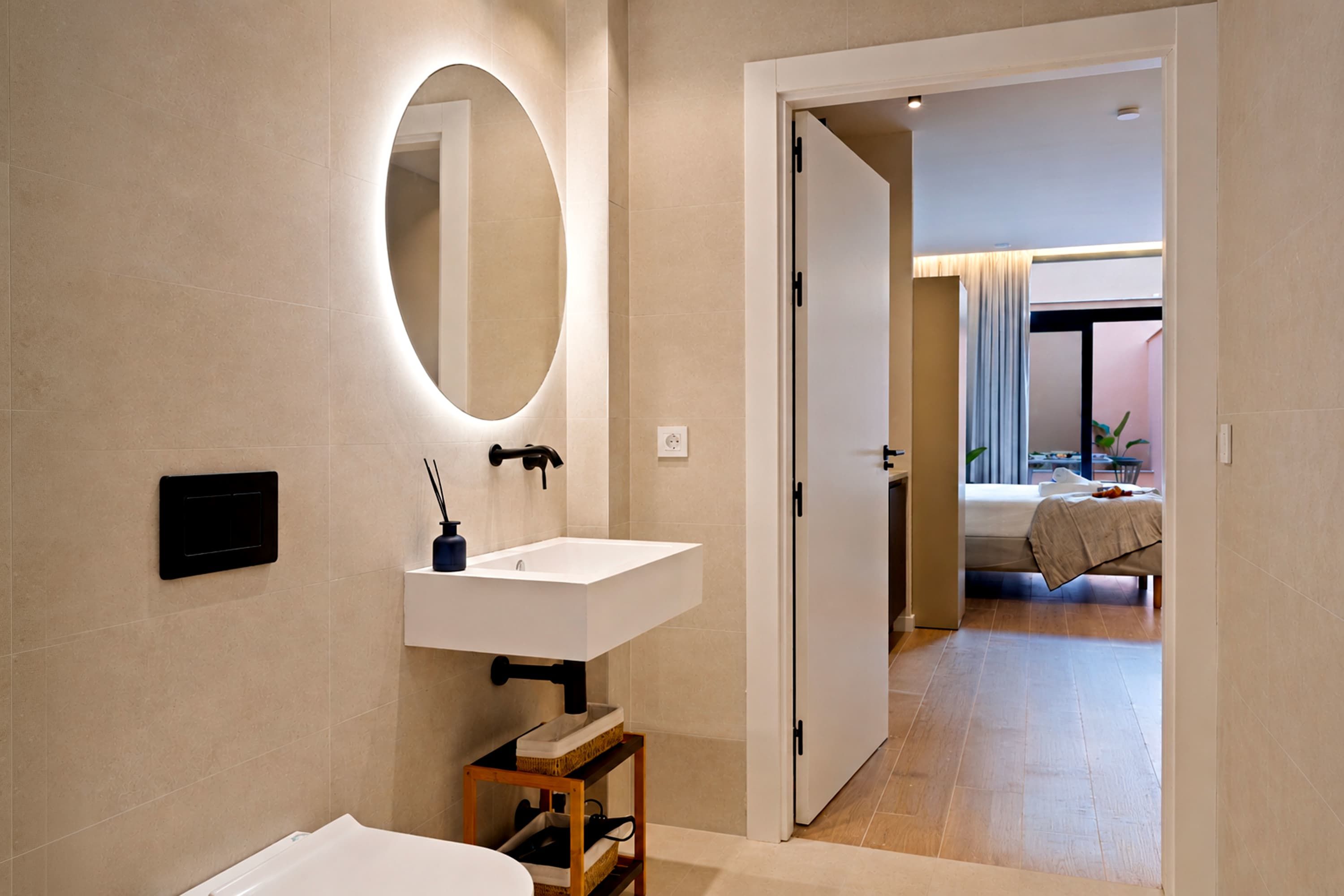 A modern bathroom with a white sink, a mirror, and a wooden stool.