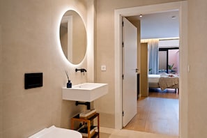 Een moderne badkamer met een witte wastafel, een spiegel en een houten kruk.