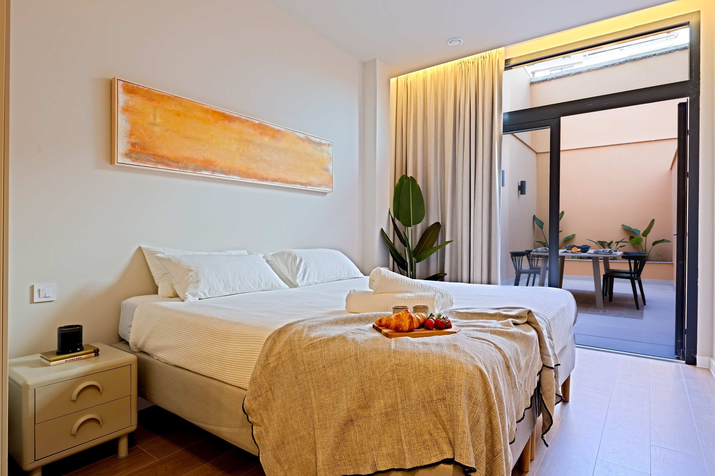 A hotel room with a bed, a nightstand, a table with chairs, and a view through a glass door.