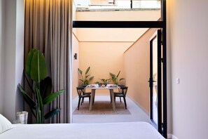 Een kamer met een bed, een eettafel met stoelen, een potplant en uitzicht op een balkon.