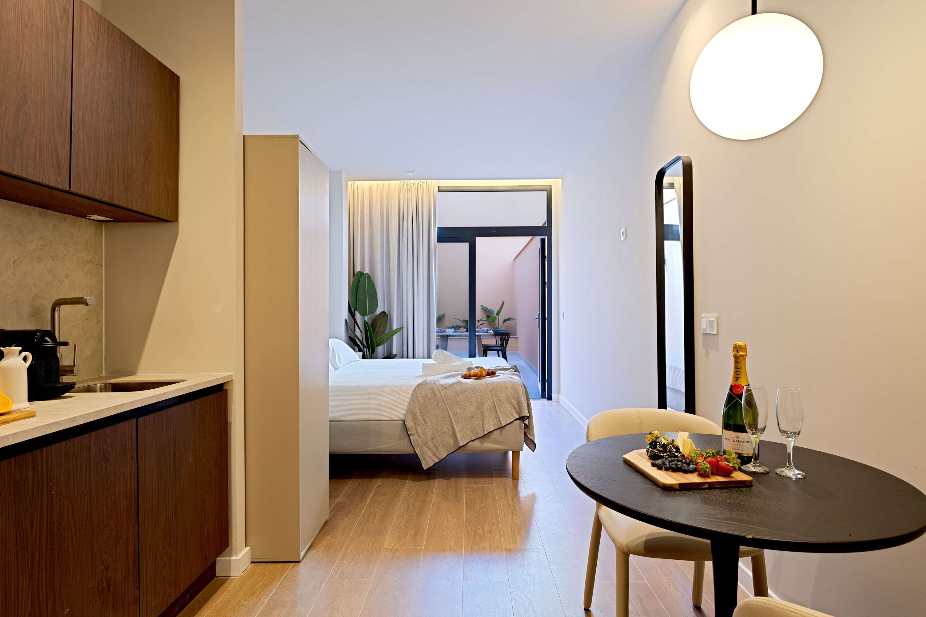 Une petite pièce comprenant un coin cuisine, un lit, une table à manger avec une bouteille de champagne et une plante en pot.