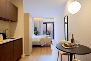 Een compacte kamer met een kitchenette, een bed, een eettafel met een fles champagne en een plant in een pot.