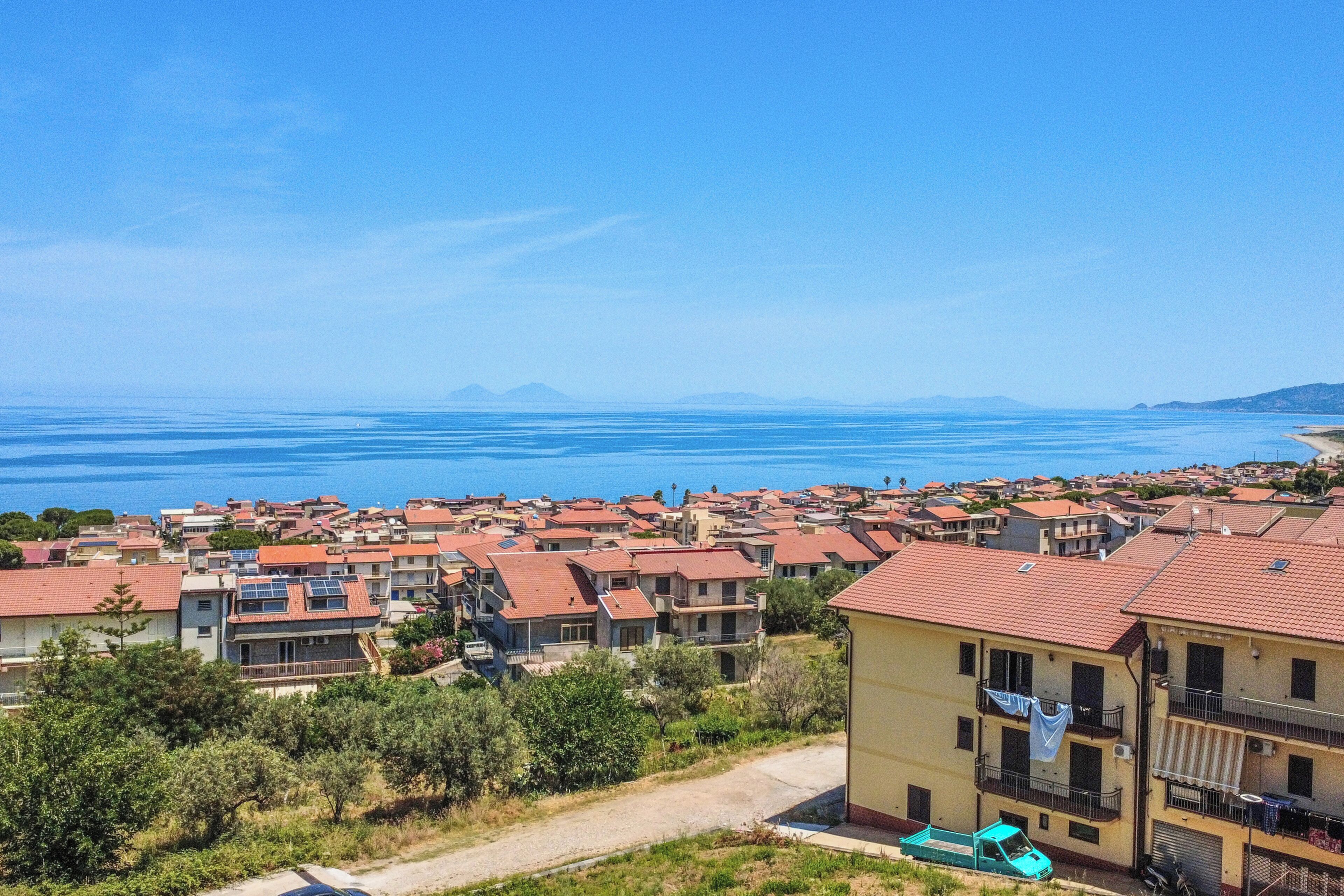 Una zona residencial costera con casas, cielo azul despejado y vista al mar.