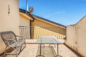 Un balcone con un tavolo in metallo e sedie in vimini, un pavimento piastrellato e un muro giallo.
