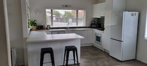 A modern kitchen with white cabinets, a built-in oven, a refrigerator, a sink, and two bar stools.