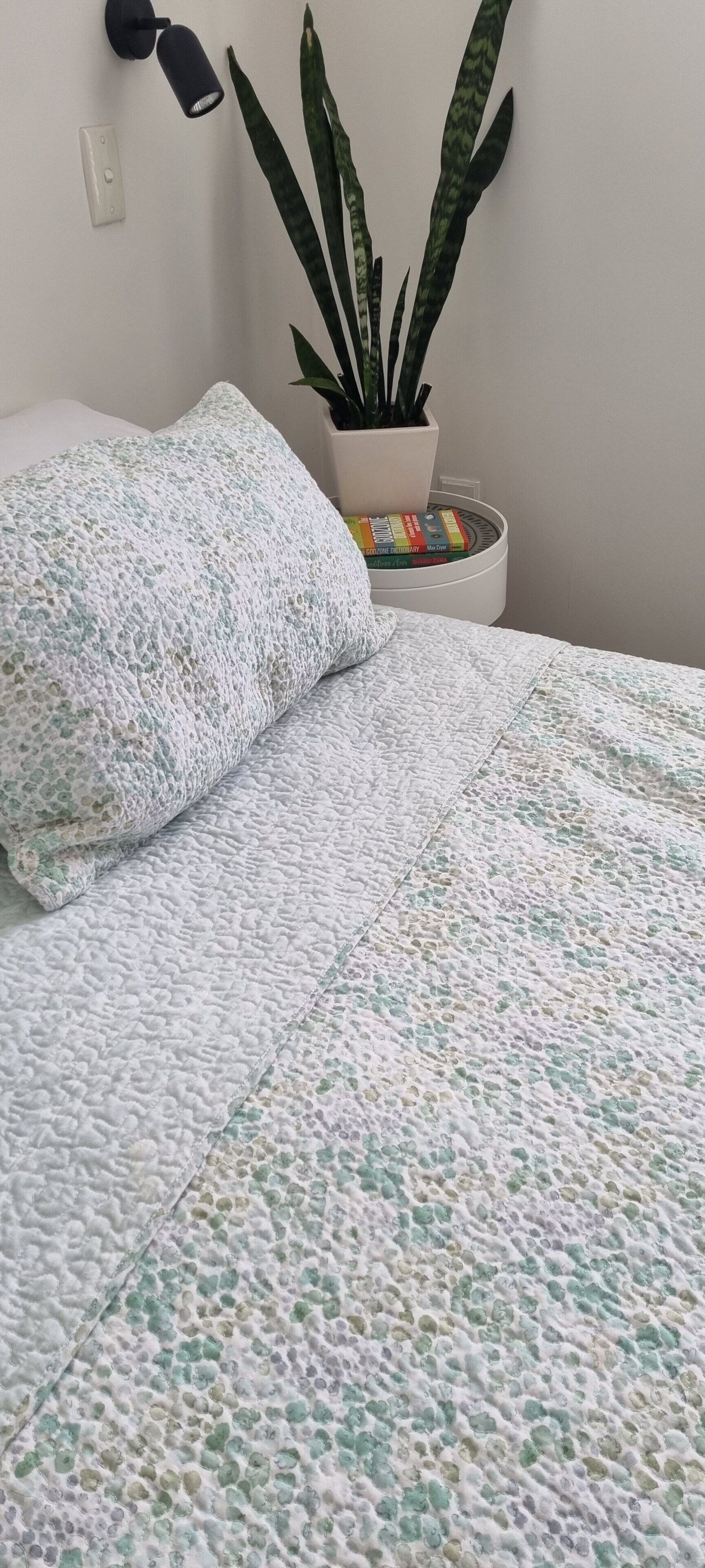 A bed with a textured blanket, a potted plant, and a wall-mounted lamp.