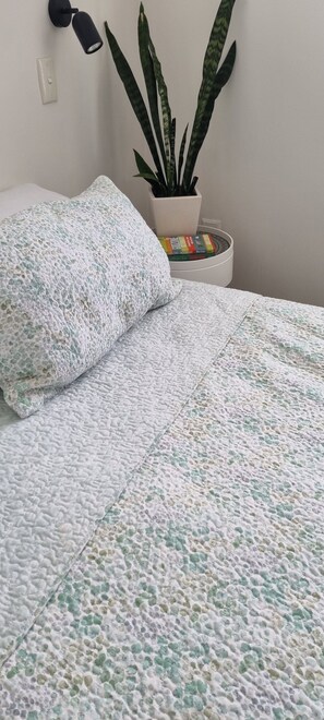 A bed with a textured blanket, a potted plant, and a wall-mounted lamp.