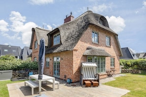 A house with a unique thatched roof, brick walls, and a patio with outdoor furniture. - Wääfblik Seestraße - Wääfblik – Your vacation home on Sylt with a sauna and ocean view (Wenningstedt-Braderup (Sylt))
