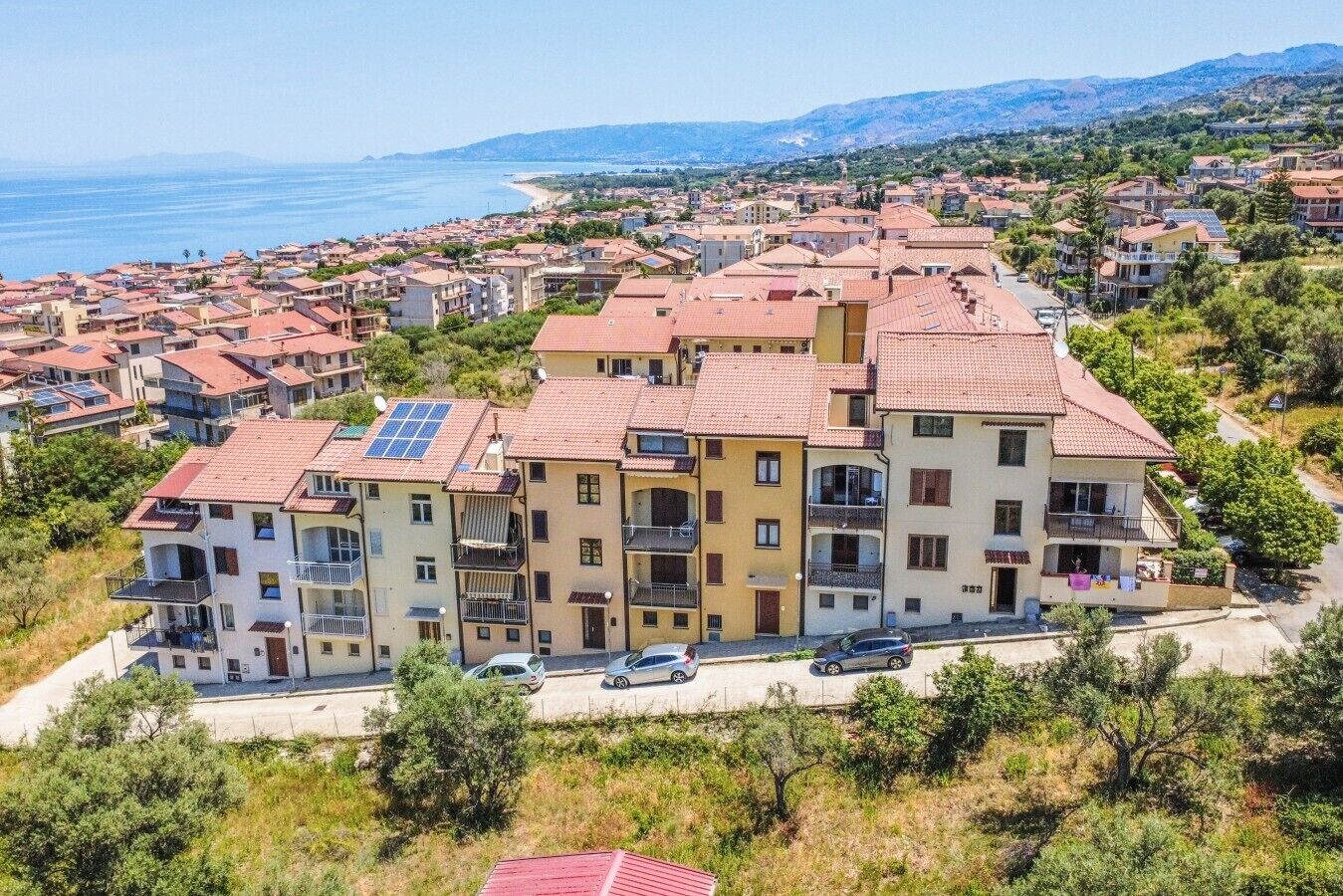 Edificio residenziale a più piani con balconi, pannelli solari e vista sul mare.