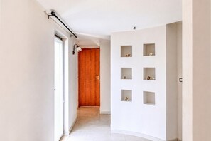 A hallway with a wooden door, a white wall with multiple empty shelves, and a ceiling track light. - Panoramics Vacation Home (Acquedolci)