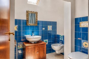 Un bagno con piastrelle blu, un mobiletto in legno, un lavandino, un bidet e uno specchio.