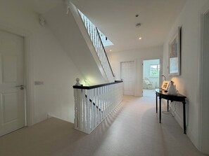 A hallway with a white staircase, a door, a small table with a picture frame, and a window. - Luxury 4BDR Retreat With Garden and Workspace (Malahide)