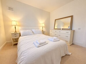 A hotel room with a bed, two bedside lamps, a dresser with a mirror, and a wall vent. - Luxury 4BDR Retreat With Garden and Workspace (Malahide)