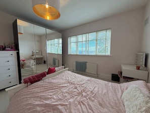 A bedroom with a large bed, a dresser, a vanity with a mirror, and a window with blinds.
